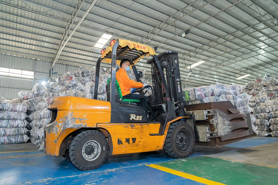 warehouse personnel moving the bales of used vintage clothing within the facility with a forklift.