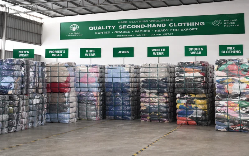 Different categories of second-hand clothing bales lined up at a wholesale warehouse showing sorted inventory ready for export