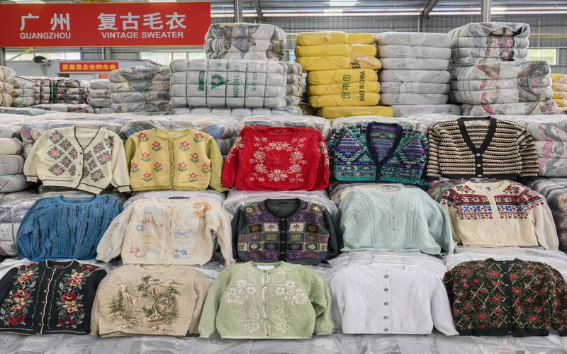 Bulk vintage knitwear bales at a sorting warehouse, colorful sweaters and cardigans stacked for wholesale export